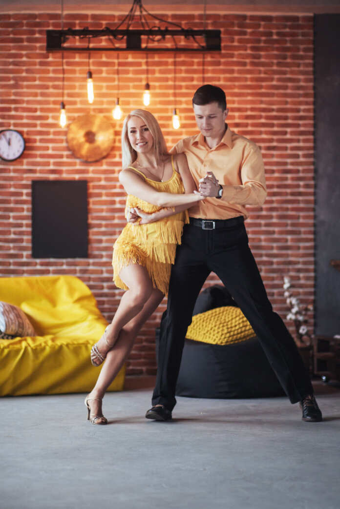 Young couple dancing latin music: Bachata, merengue, salsa. Two elegance pose on cafe with brick walls
